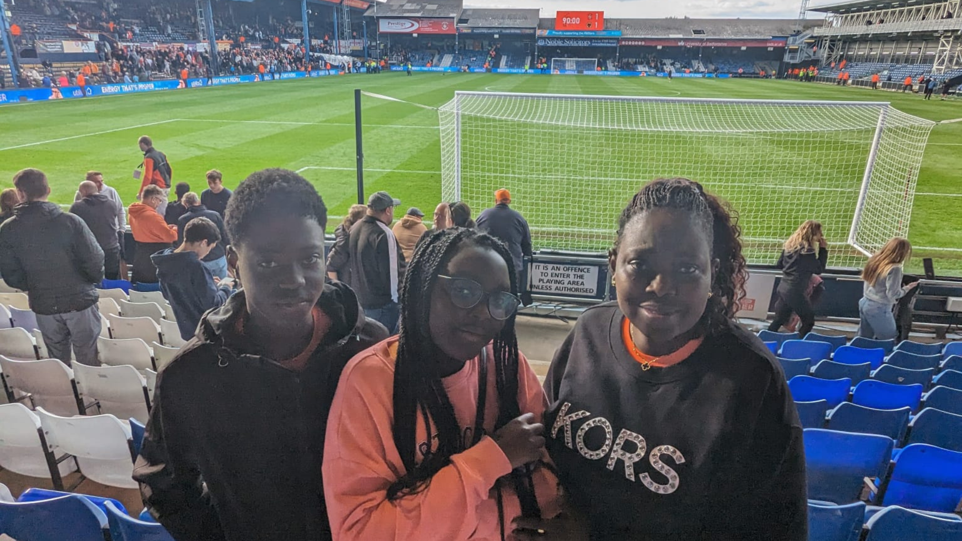 Young carers at the Luton match on Saturday, stood in front of the football pitch and smiling at the camera