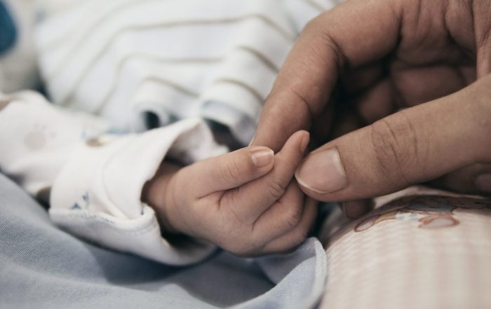 Hands of a adult, gently holding the fingers of a baby.