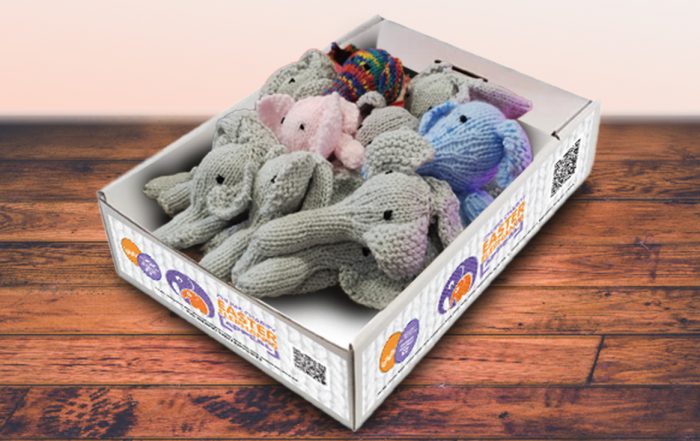 Knitted elephants laid out in a branded display box with the CHUMS logo on